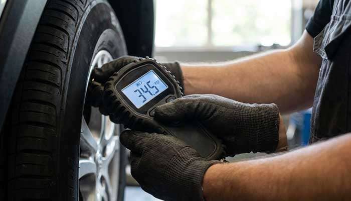 Person wearing gloves holding a digital tire pressure gage showing 29.0 psi near a car tire