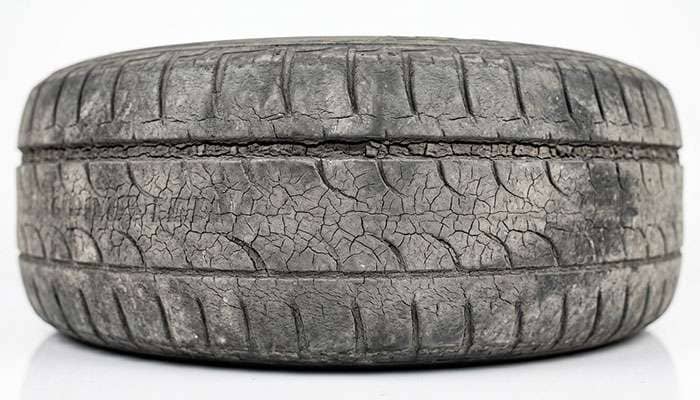 Close-up of dry rot cracking across the sidewall and tread grooves of an aged tire