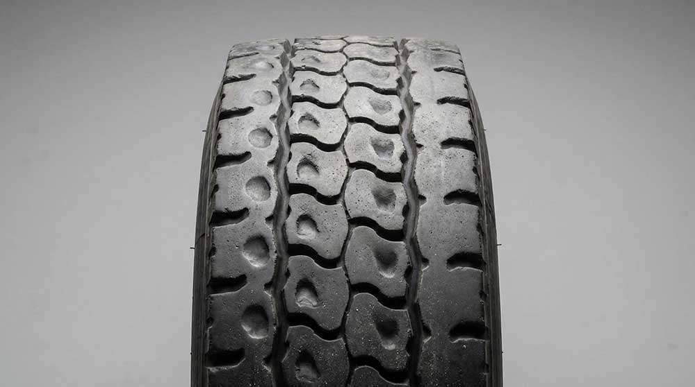 Close-up of a commercial tire showing irregular and uneven tread wear patterns