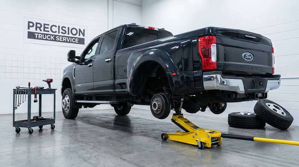 Maroon and tan truck with a raised rear wheel being replaced, showing tools, tires, and parts on a driveway
