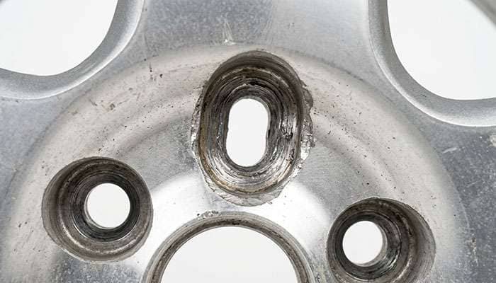 close-up of an elongated out of round lug hole on an aluminum wheel caused by driving with a missing lug nut