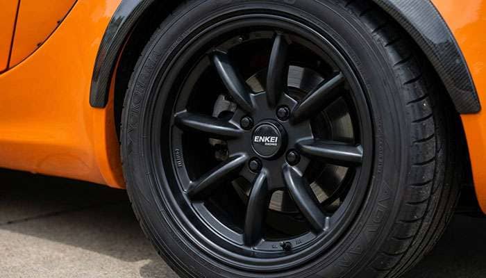 Close-up of a matte black Enkei COMPE wheel with Yokohama tire on an orange car with carbon fiber fender flare