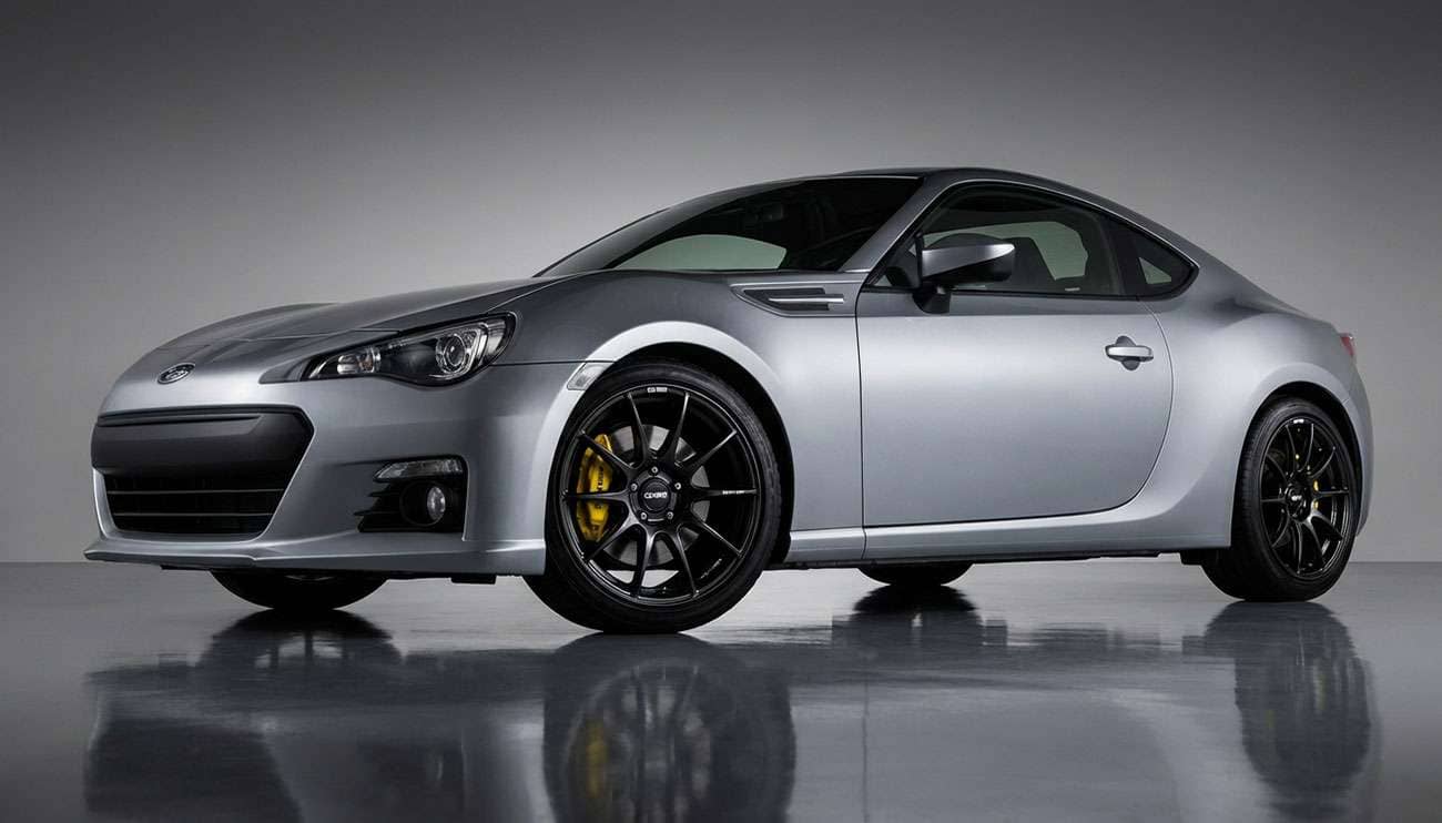 Sleek silver sports car with glossy black Enkei rims and yellow brake calipers on a reflective floor