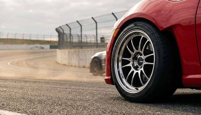 Close-up of a red car featuring Enkei wheels on a racetrack