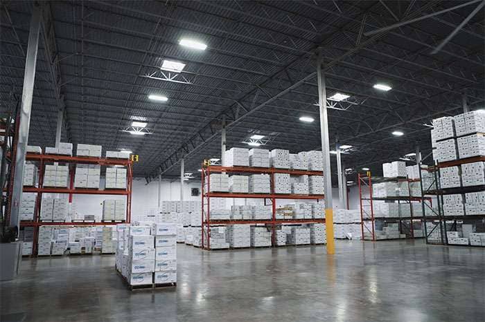 Large warehouse interior filled with stacked white Enkei Wheels boxes on pallets and orange metal shelving units