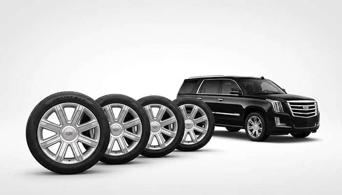 Set of four 22-inch Cadillac Escalade ESV OEM design wheels with tire size 285/45 R22 shown next to a black Escalade SUV.