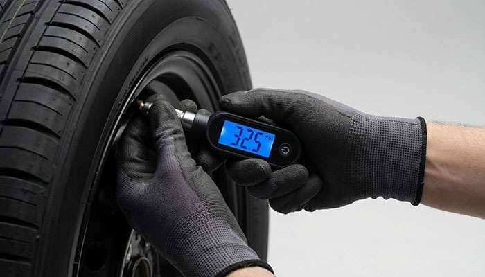 Person wearing gloves using a digital tire pressure gage to check a car tire's pressure at 29.0 PSI