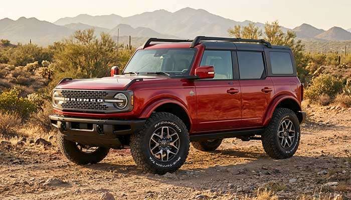 Red Ford Bronco equipped with large 35-inch off-road tires parked outdoors on a dirt surface