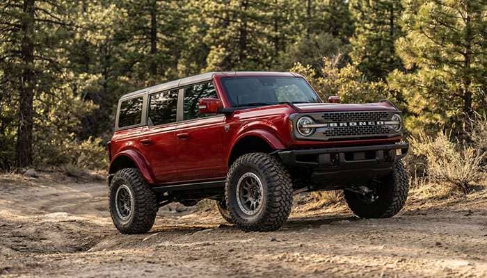 Red Ford Bronco with large 35-inch off-road tires parked on a dirt surface surrounded by trees