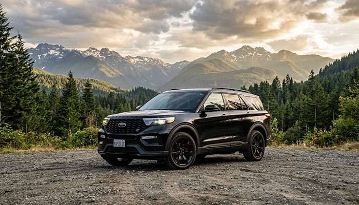 Black Ford Explorer ST parked on gravel with mountains and trees in the background on a partly cloudy day
