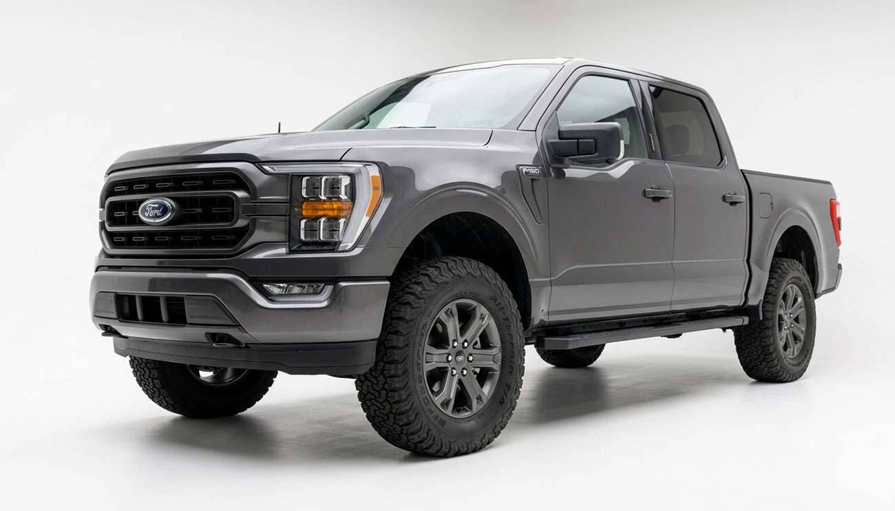 Full-size pickup truck on stock suspension fitted with oversized all-terrain tires, front three-quarter view showing the front wheel opening