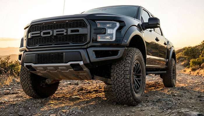 Close-up of a black Ford F-150 truck showcasing its rugged off-road tires and front grille in daylight