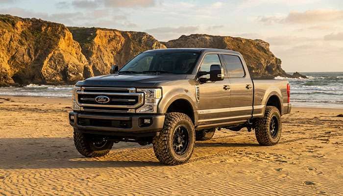 2023 gray Ford F-250 Super Duty leveled on large off-road tires parked on a sandy beach near ocean cliffs.