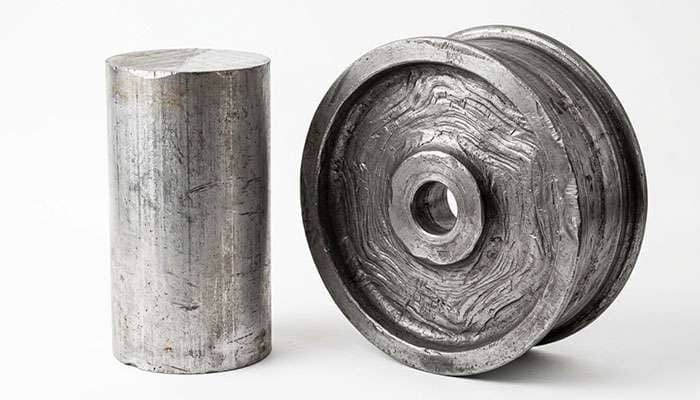 Solid aluminum billet beside a rough forged wheel blank showing compressed grain structure before machining