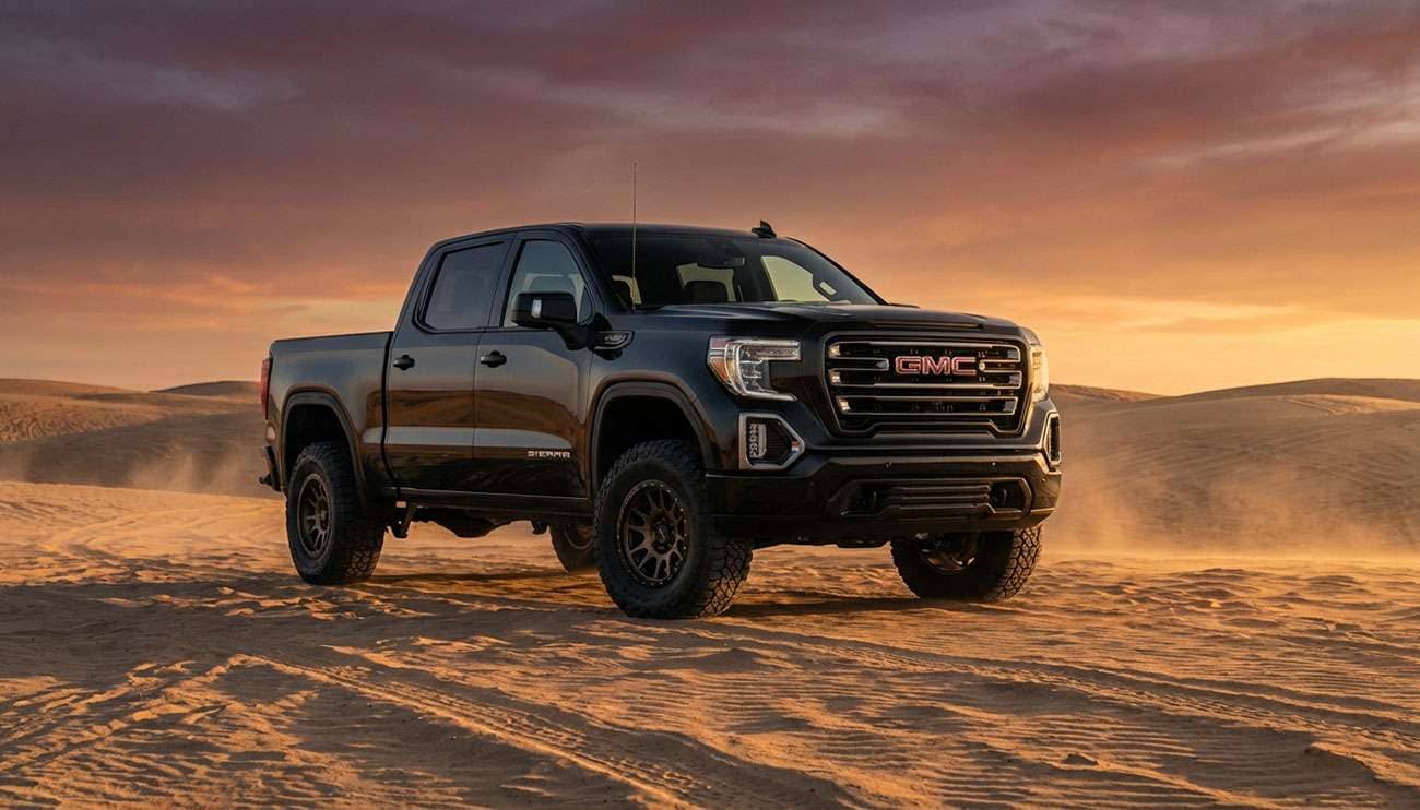 Black GMC Sierra 1500 pickup truck with aftermarket off-road wheels parked on sandy terrain at sunset