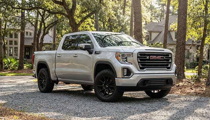 Silver GMC Sierra 1500 truck parked on driveway with custom black rims and off-road tires in a wooded area