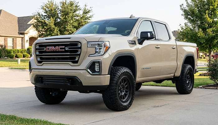 Beige GMC Sierra truck with black 35-inch tires on stock suspension parked in a residential driveway