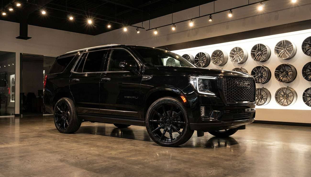 Sleek black GMC Yukon with aftermarket black wheels displayed in a modern showroom with wheel options on the wall