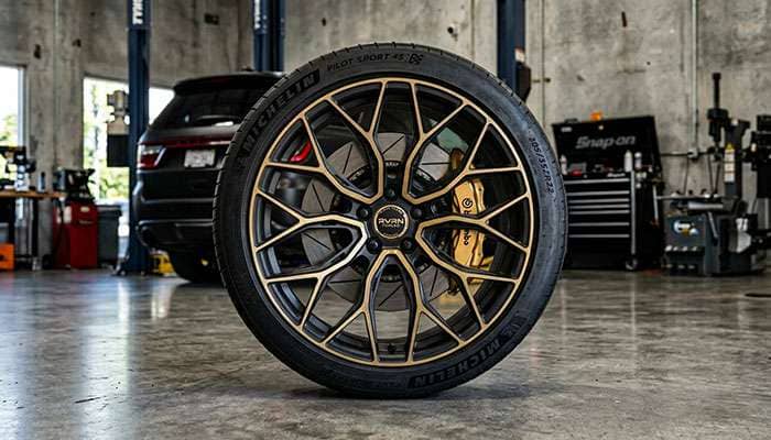 Gold and black RVRN forged custom wheel for Dodge Durango displayed in a garage setting.