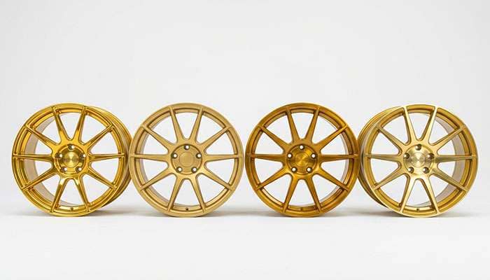 Four gold alloy wheels showing gloss, matte, brushed candy, and machined gold finishes on a white studio backdrop