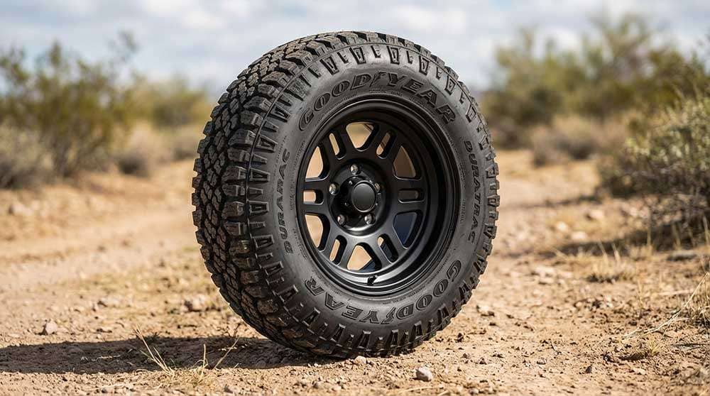 Close-up of a Goodyear Wrangler DuraTrac Rugged Terrain tire mounted on a black off-road wheel on dirt ground