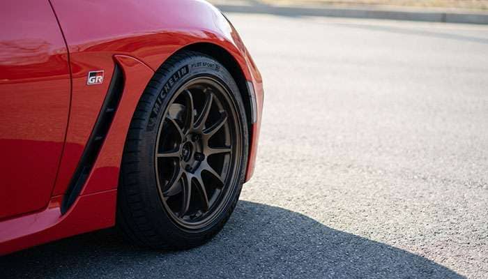 Close-up of a red sports car rear wheel with performance tire on asphalt surface