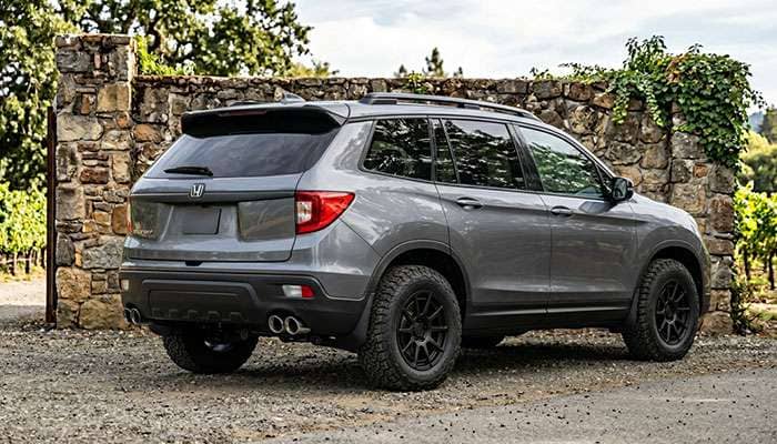 Side view of a gray Honda Passport SUV with black aftermarket wheels parked in front of a stone wall.