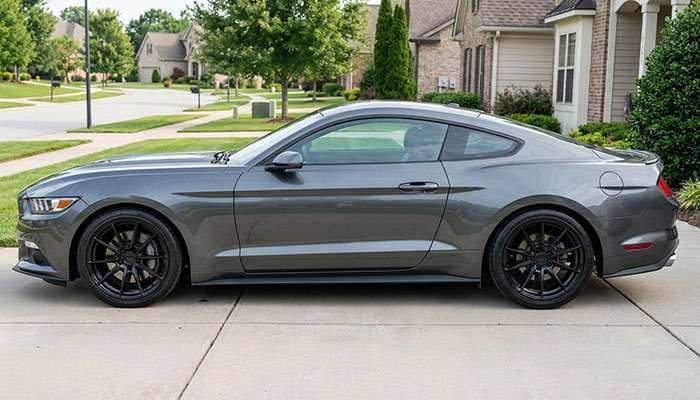 Side view of a gray S550 Mustang with aftermarket wheels parked on a driveway in a residential area