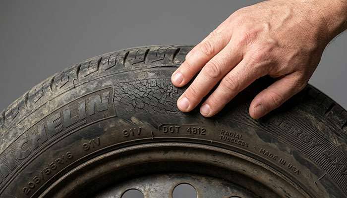 Hand inspecting aged car tire sidewall for cracks and dry rot before remounting