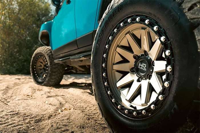 Close-up of a Hardrock Offroad wheel with a detailed bolt pattern on a blue off-road vehicle in sandy terrain