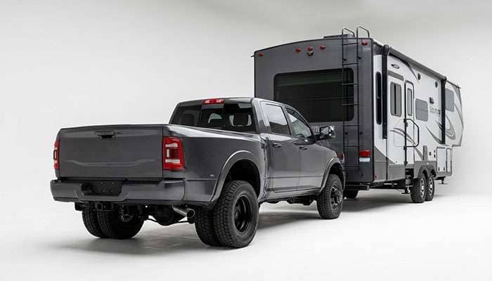 Heavy duty pickup truck towing a fifth wheel trailer, rear axle loaded, viewed from behind on a highway