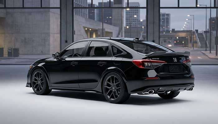 Black Honda Civic showcasing dual chrome exhaust tips, a carbon fiber spoiler, and sharp wheel fitment in an urban setting
