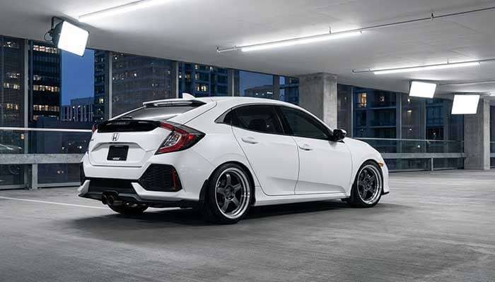 Rear view of a white Honda Civic hatchback with an aftermarket spoiler and deep-dish wheels in a modern urban setting