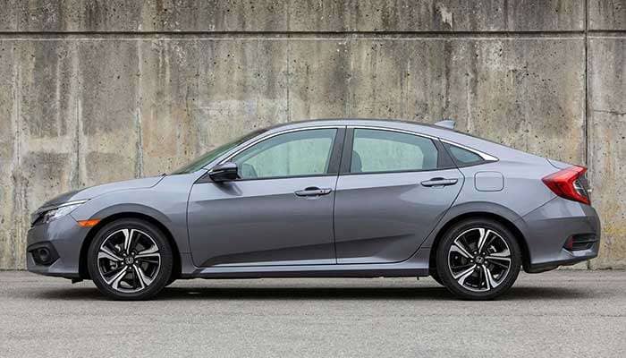 Side view of a gray Honda Civic with black and silver alloy wheels, parked against a textured concrete wall outdoors