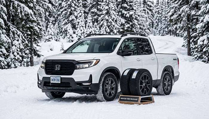 White Honda Ridgeline truck with winter tire packages displayed against a snowy forest background.