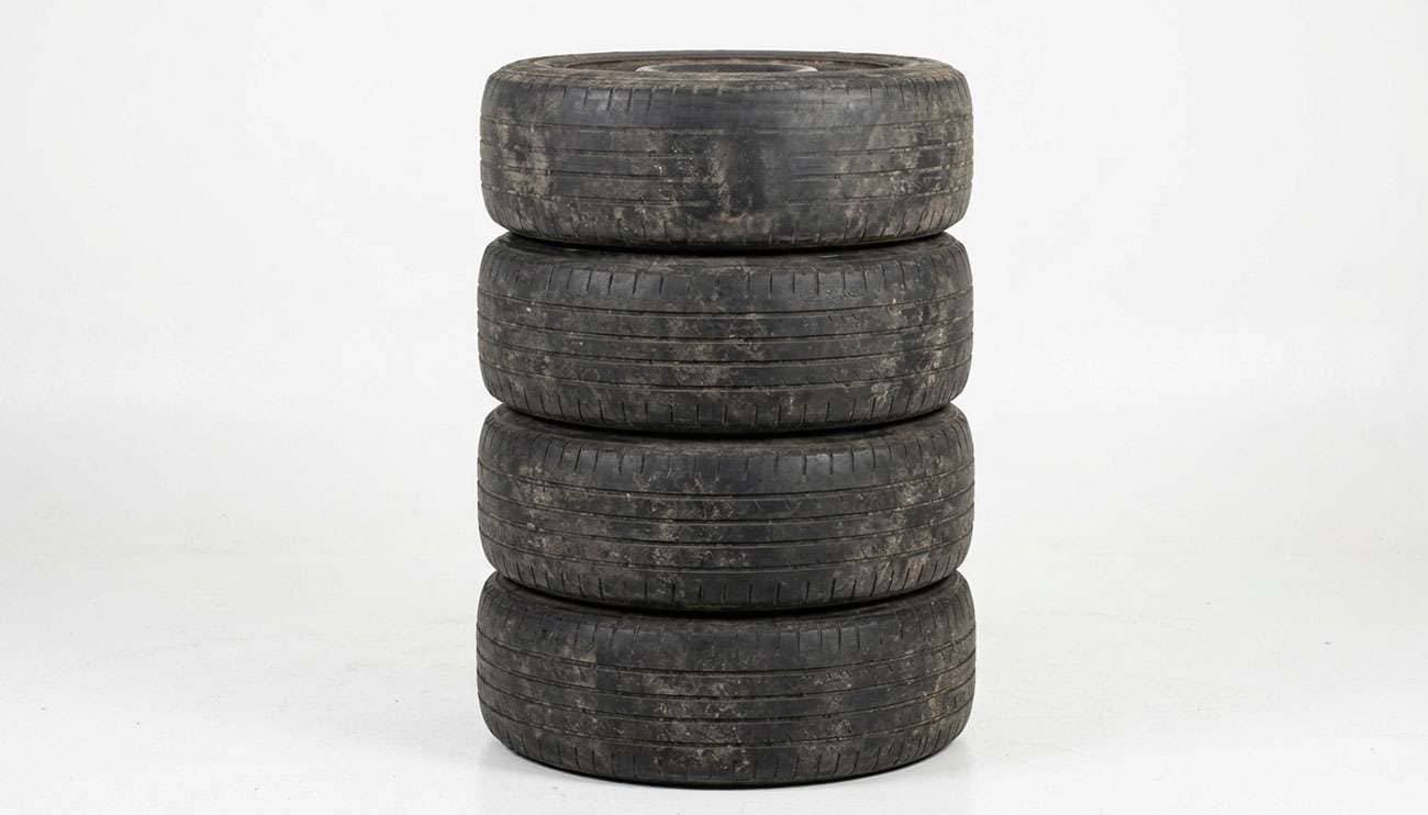 Stack of worn passenger tires beside a garage wall awaiting legal disposal