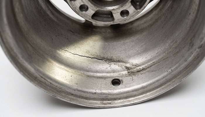 Close-up of a hairline crack in the inner barrel of a dismounted aluminum wheel under bright inspection lighting