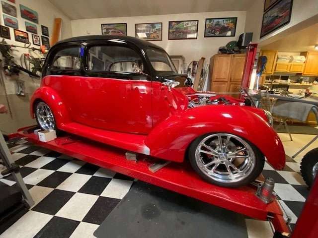 Red and black 1934 Ford with shiny retro XLR wheels displayed indoors on a red platform in a garage