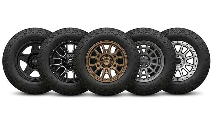 Multiple Jeep Wrangler aftermarket wheel designs displayed together showing matte black, gloss black, and bronze finish options.