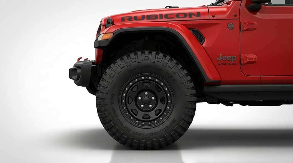 Close-up of a black steel wheel with off-road tire on a red Jeep Wrangler Rubicon against white background