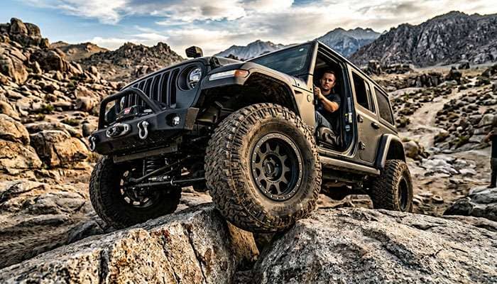 Jeep Wrangler with beadlock aftermarket wheels crawling over large boulders at low tire pressure on an extreme off-road trail.