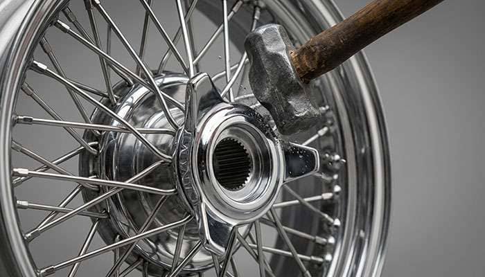 Lead hammer striking the ear of a chrome knockoff spinner on a classic car wheel