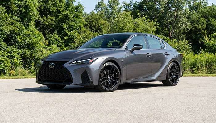 Gray Lexus IS500 sedan with custom black wheels parked on pavement with green trees in the background