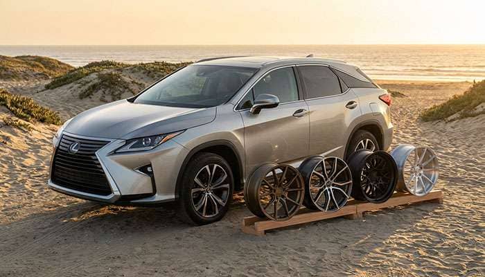 Silver Lexus SUV parked by the beach with four different aftermarket wheel designs displayed beside it