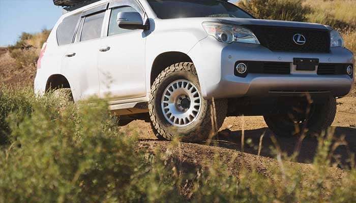 Silver Lexus SUV equipped with Nomad Wheels driving off-road on a dirt trail with vegetation in the foreground