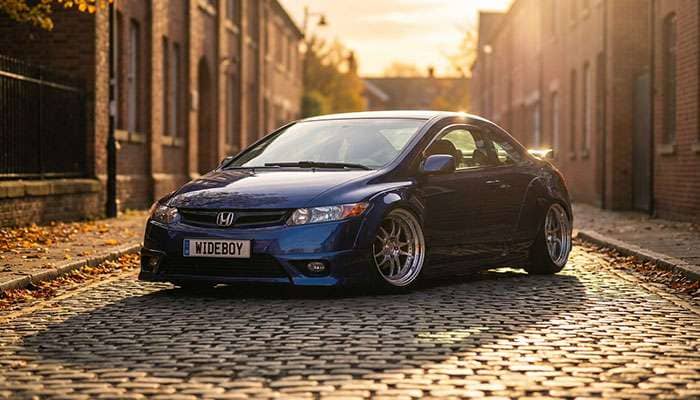 Lowered dark blue 8th gen Honda Civic with wide stance and deep-dish wheels parked on a street curve