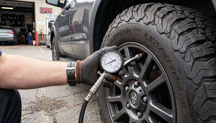 Technician checking the pressure of an LT275/70R18 all-terrain tire on a Toyota Sequoia with a dial tire gauge