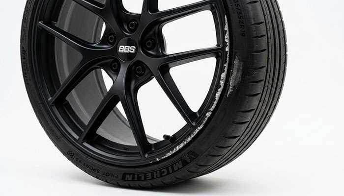 Matte black wheel showing curb rash and a scuff on the outer lip