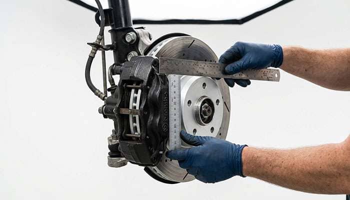 Technician using a straight edge and millimeter rule to measure brake caliper height and width from the hub mounting face