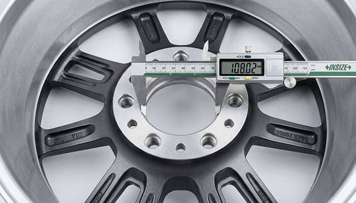 Digital calipers measuring the center bore of a six-lug truck alloy wheel